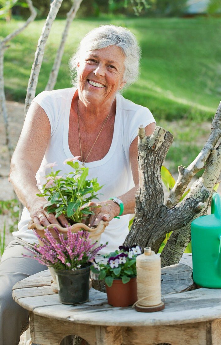 Ältere Frau arrangiert Blumen auf einem Gartentisch