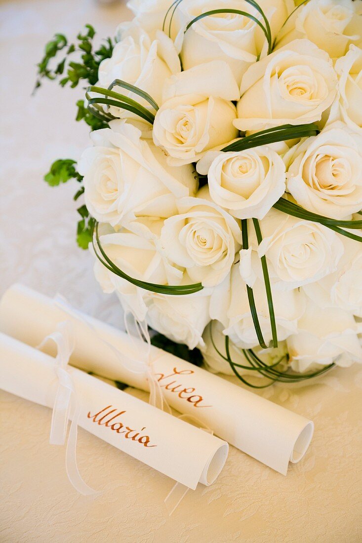 White bridal bouquet behind scrolls of paper bearing names of bride and groom