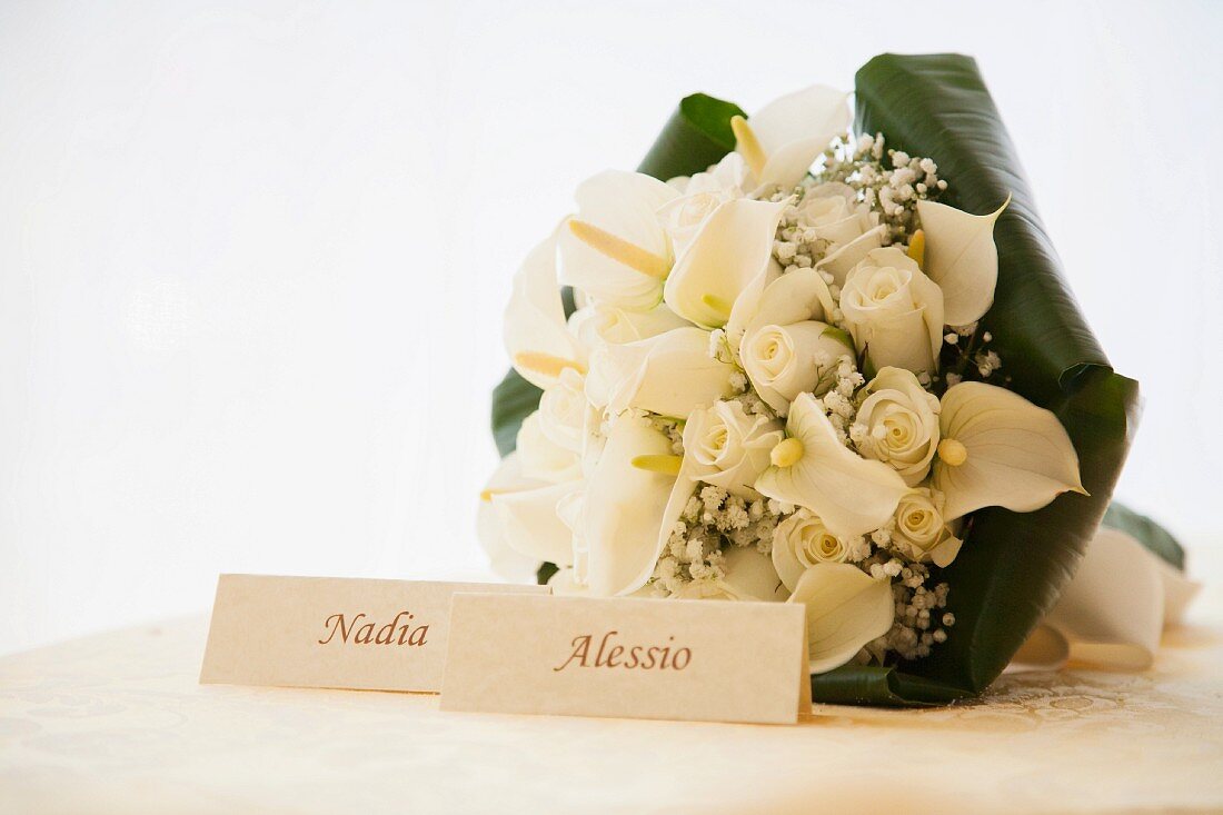 Bridal bouquet with roses and calla lilies behind cards bearing names of bride and groom