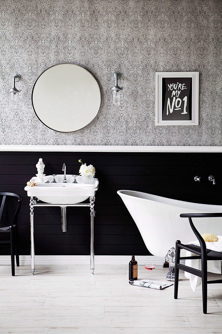 Waschtisch mit Chromgestell und Badewanne vor teilweise schwarz getönter Wand, oberhalb tapeziert mit grauem Muster