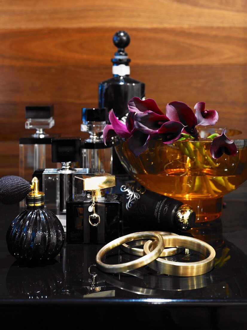 Verschiedene edle Flacons, Schale mit Orchideenblüte und Armreif auf schwarzem Schminktisch