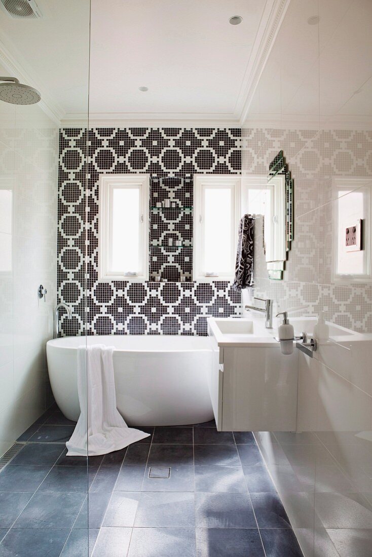 Modernes Bad mit Waschtisch an hochglänzender Wand und freistehende Badewanne vor gefliester Wand mit schwarz-weißem Ornamentmuster