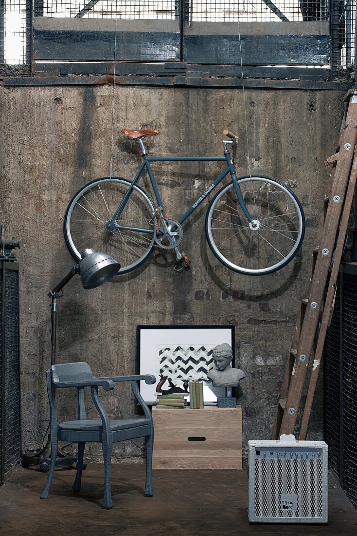 Armlehnstuhl, Retrolampe, Bild und Frauenbüste mit aufgehängtem Fahrrad vor alter Kellerwand
