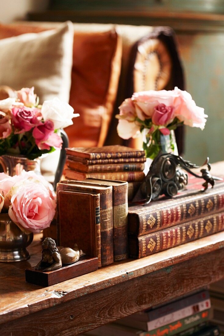 Antiquarian books with gilt-embossed leather bindings, antique bookend and posies of roses on old wooden shelf