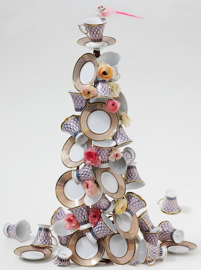Weihnachtsbaum-Pyramide aus gemusterten Porzellantassen und Tellern mit Blütendeko