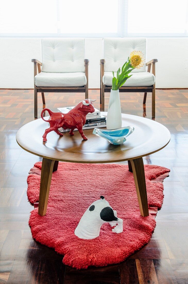 Runder Holztisch auf rotem stilisiertem Tierfellteppich und roter Stierfigur als Tischdeko