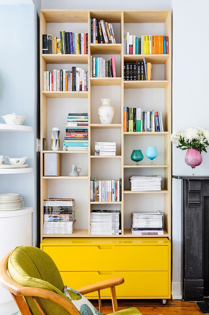 Shelving in niche above bright yellow drawers as modern element between rounded kitchen shelving and antique fireplace surround