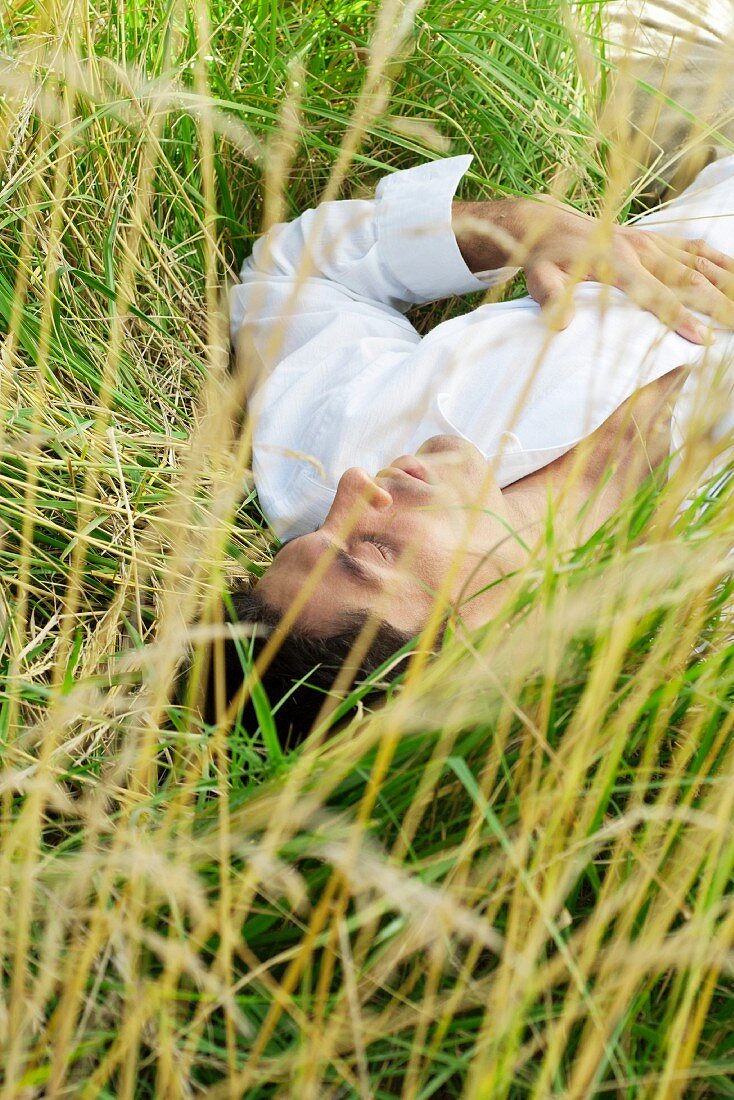 Man lying in tall grass with eyes closed