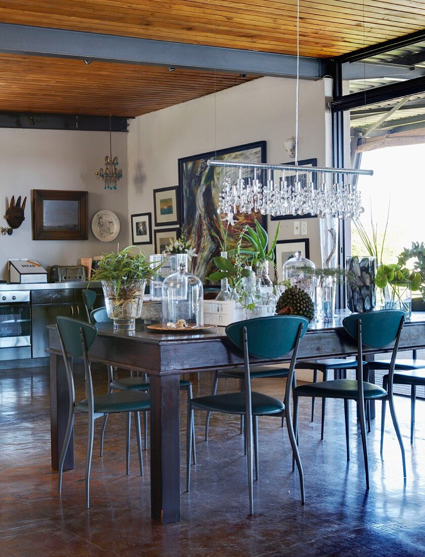 Delicate metal chairs around rustic dining table with collection of glass vessels used as planters in simple interior