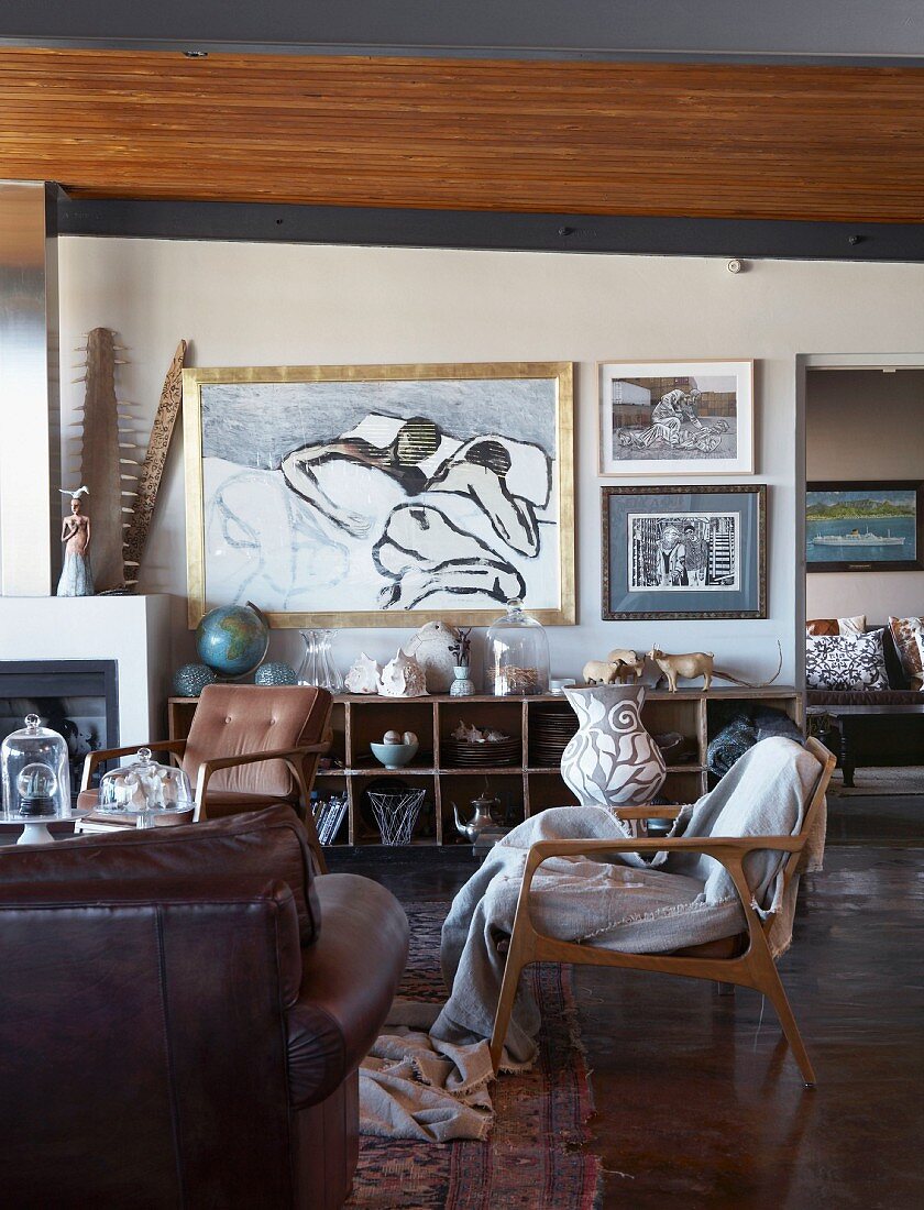 Wohnbereich mit verschiedenen Sesseln im 50er Jahre Stil, im Hintergrund moderne Malerei über offenem Regalschrank an Wand