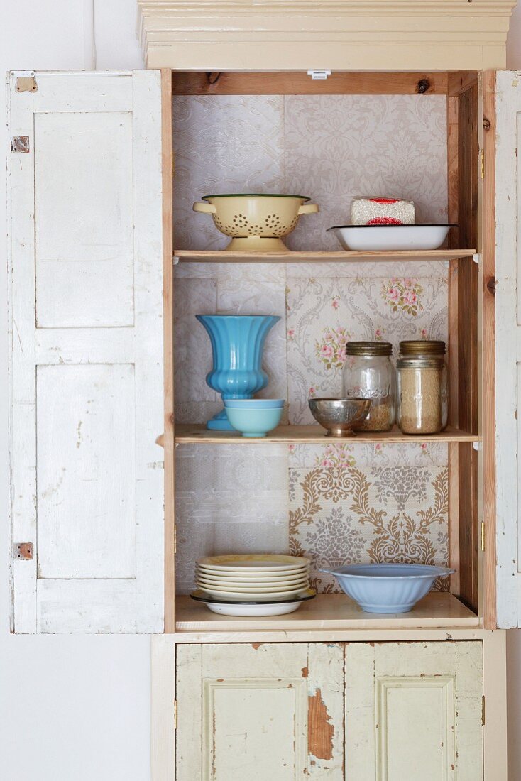Vintage Küchenschrank mit tapezierter Rückwand, offener Tür und Blick auf Geschirr