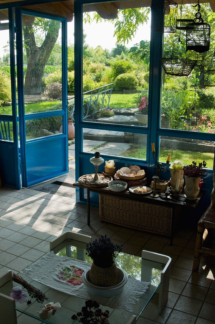 Mediterraner Wohnraum mit Couchtisch auf weißem Fliesenboden vor Wandtisch an Terrassenfenster mit Blick auf angelegtem Garten