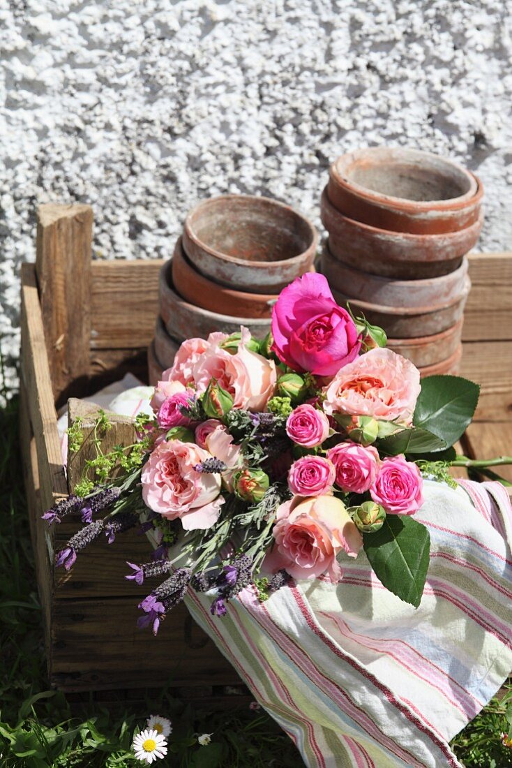 Bouquet of roses, striped tea towel and old flowerpots in simple wooden crate