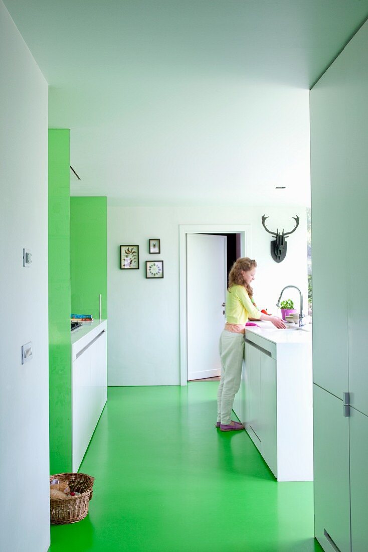 Woman in open-plan white, designer kitchen with green floor