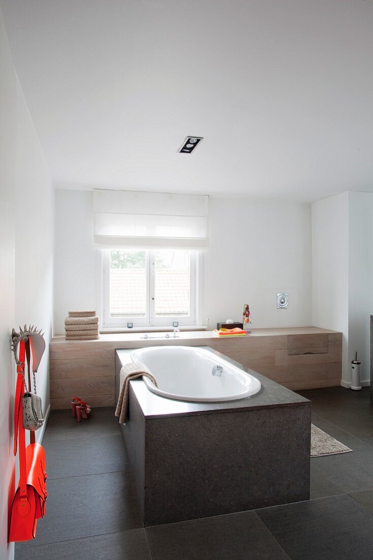 Free-standing, stone-clad bathtub in front of window in minimalist bathroom