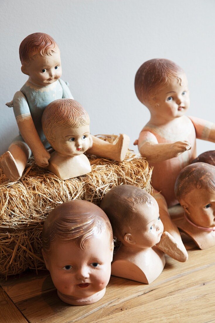 Arrangement of old dolls, dolls' heads and miniature bale of straw