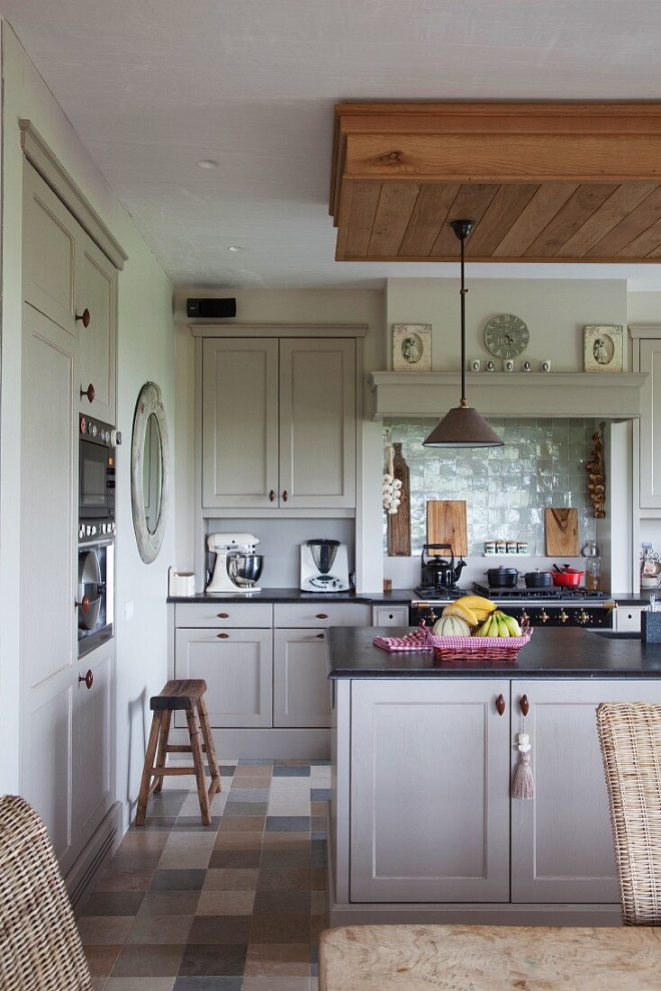 Bright, Shaker-style, country-house kitchen with sink unit and old wooden stools on marble floor tiles in natural shades