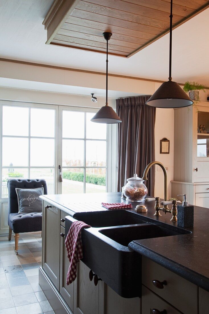 Kitchen counter with pale, painted, Shaker-style cupboards, dark double sink and brass retro tap fittings