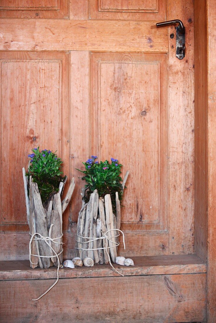 Originelle Blumentöpfe aus verschnürtem, hellem Treibholz vor alter Landhaustür