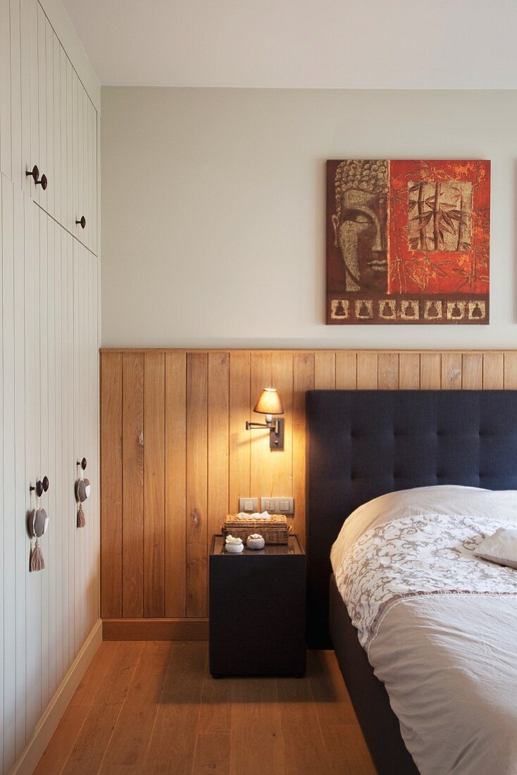 Double bed with charcoal upholstered headboard against oak wood panelling and white fitted wardrobe to one side
