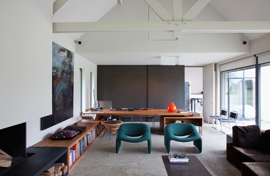 Spacious living room with exposed roof structure and desk built into low, fitted wooden cabinets running along one wall