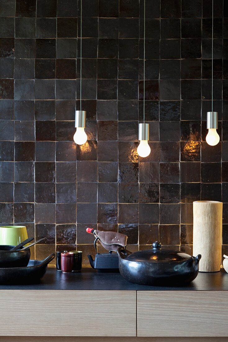Small, simple pendant lamps in front of elegant charcoal wall tiles in architect-designed kitchen