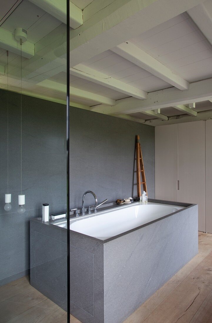 Bathtub in free-standing, grey stone cube in designer bathroom with historical wooden ceiling