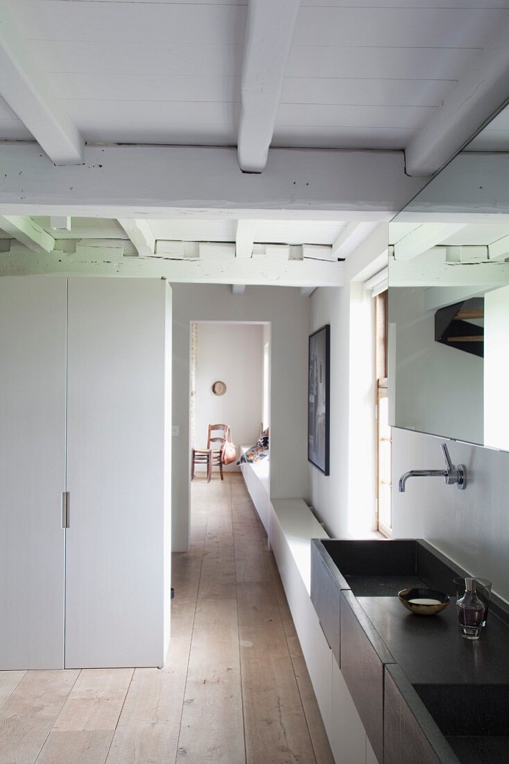 View past dark grey twin washstand in bathroom into corridor