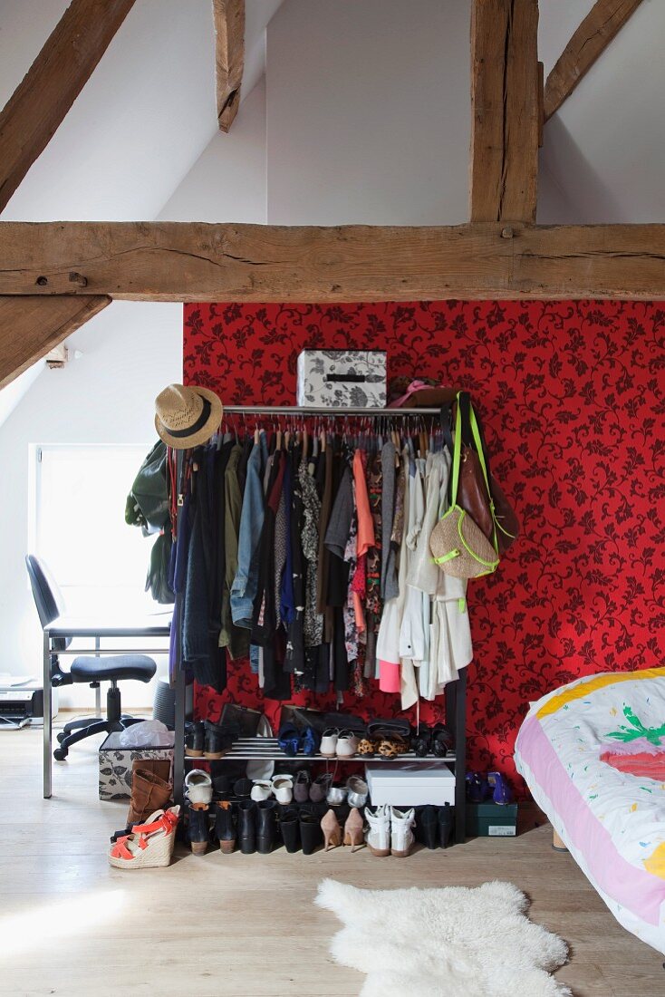 Teenager's room with exposed roof structure, clothing rack and open shoe rack against patterned wall