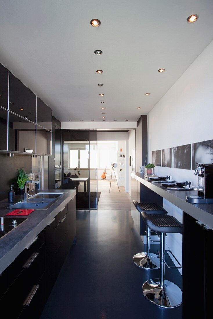 Offener Küchenbereich mit Barhockern an Frühstückstheke gegenüber Einbauküchenzeile und Blick ins Wohnzimmer