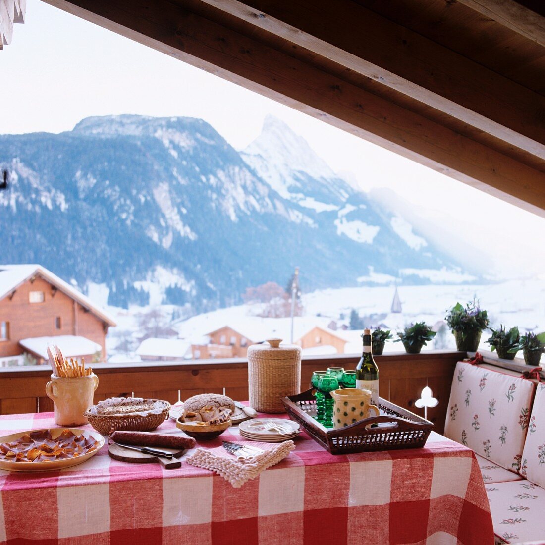 Table set for simple lunch in loggia of chalet with view of snowy mountain landscape