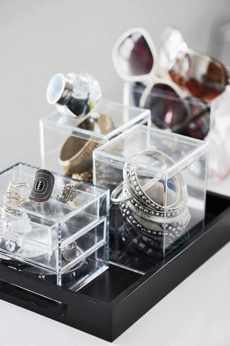 Small plexiglas boxes used to store jewellery and glasses on black tray