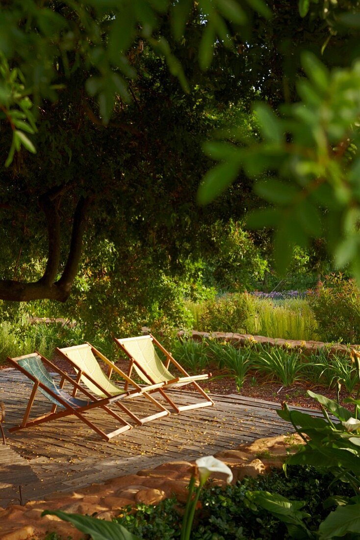 Stoffbespannte Liegestühle in der Abendsonne auf einem Holzdeck im Garten