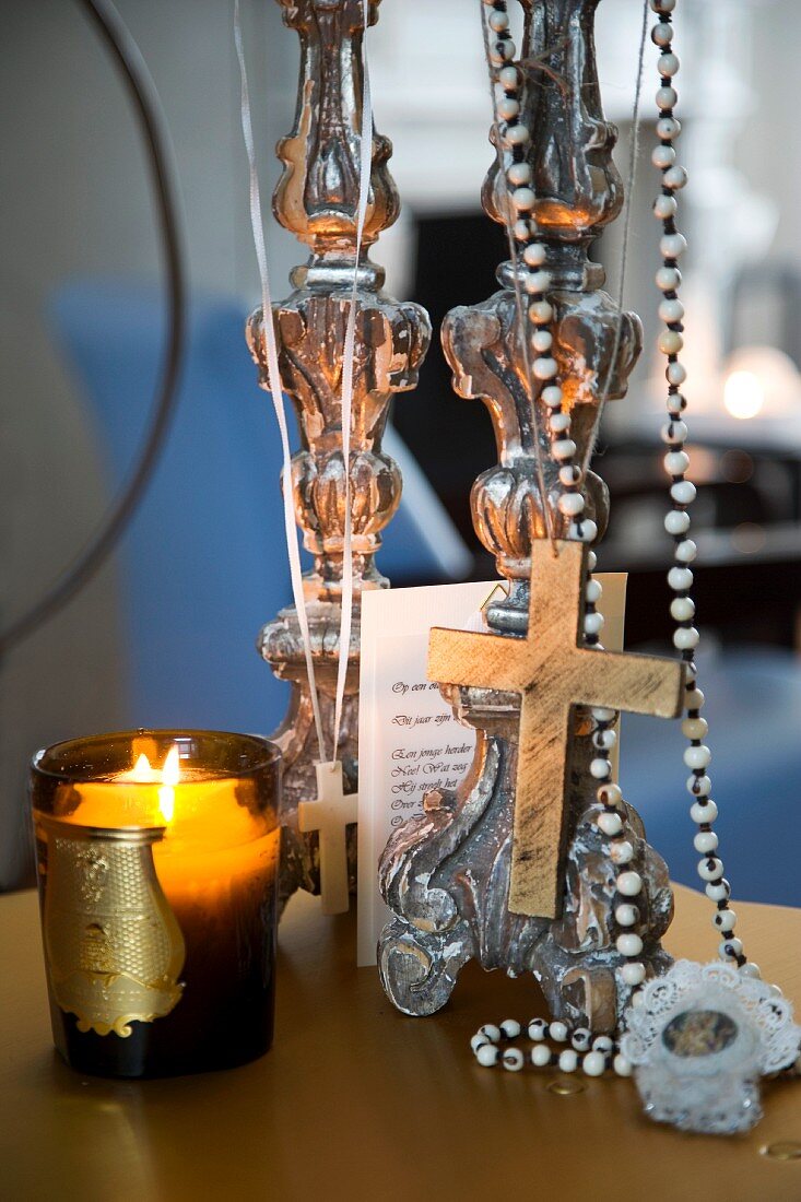 Windlicht mit brennender Kerze neben aufgehängter Halskette mit Kreuzanhänger
