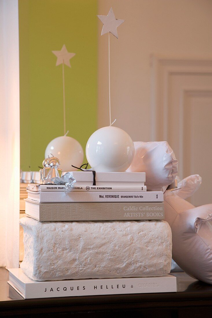 White, decorative, spherical candles with stars on stacked books in front of bright green stripe on wall