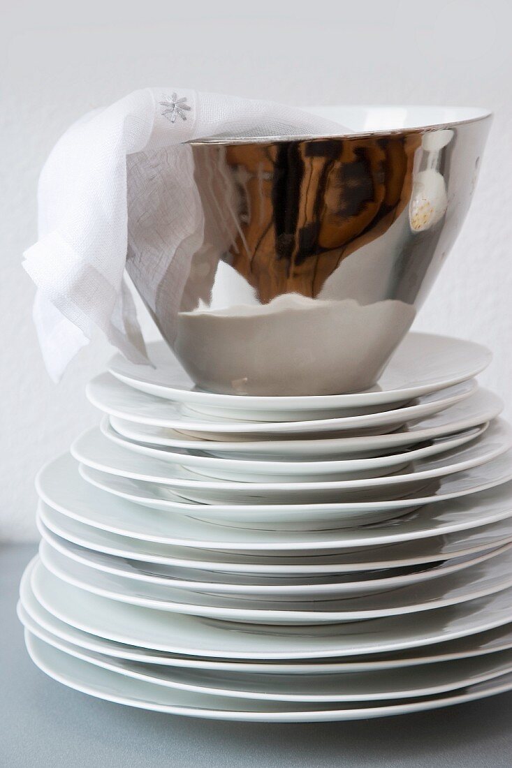 Linen napkin in silver china bowl on stack of white plates against white wall