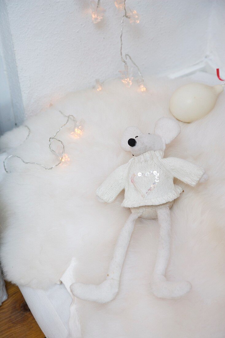Detail of mattress with white soft toy on fur blanket and string of fairy lights
