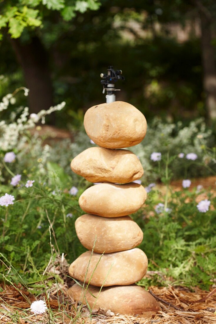 Aufgestapelte, runde Steine vor einer Wasserleitung im Garten