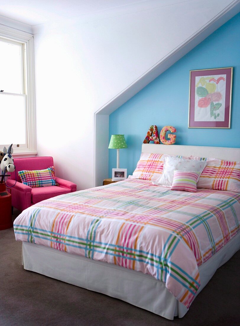Kinderzimmer unterm Dach mit farbenfroh karierter Bettwäsche vor hellblauer Wand