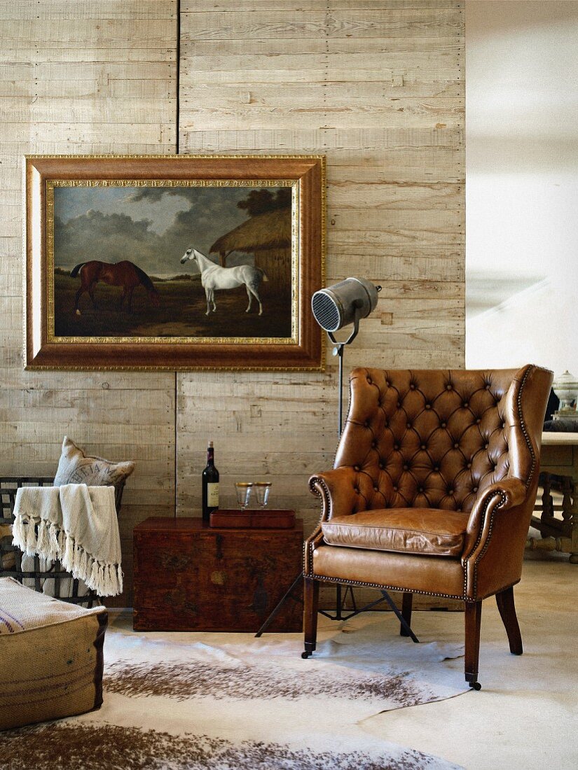 Antique leather armchair in front of wooden partition and picture of horses