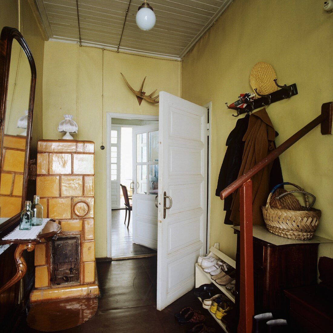 Offene Garderobe und Schuhregal gegenüber Spiegel mit Ablage und gemauerter Kamin mit gelben Fliesen im Vorraum