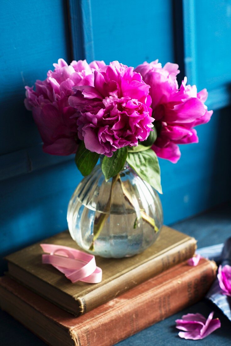 Pink peonies in a glass vase on antique books