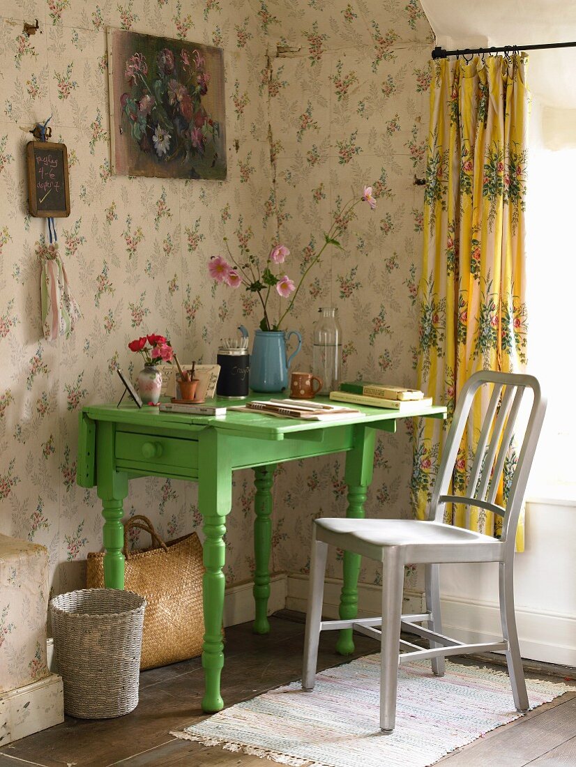 A small green desk in the corner of a room with floral wallpaper
