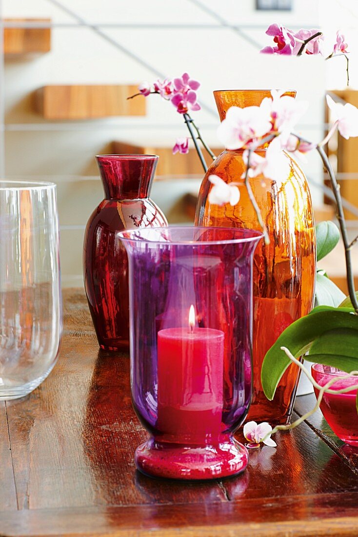 Colorful hurricane candle, glass vases and orchids on a table
