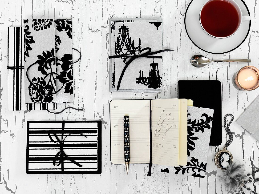 In black and white: wrapped presents, a notebook, a medal, a candle and a cup of tea, all on a wooden surface