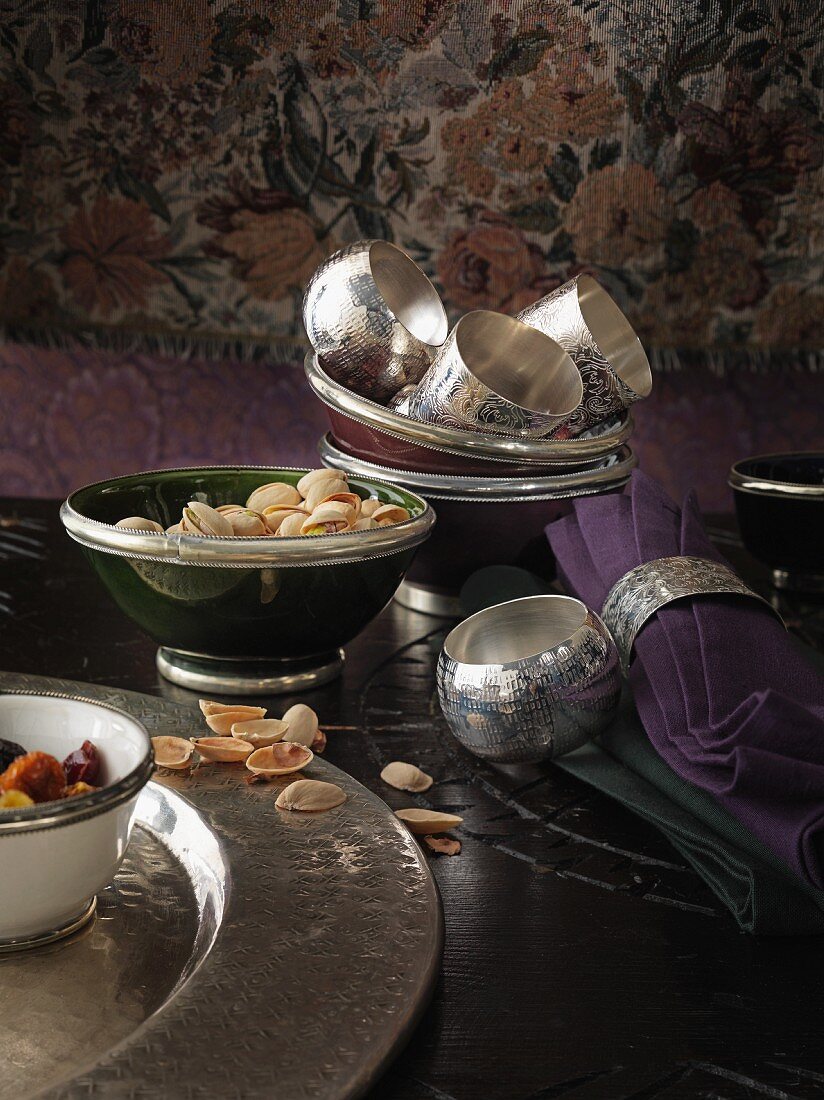 Silberne Serviettenringe, Stoffserviette und Schale mit Pistazien auf einem dunklen Tisch
