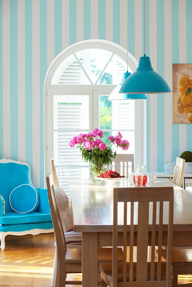 Esstisch mit Holzstühlen und blauer Polsterstuhl vor einem Rundbogenfenster