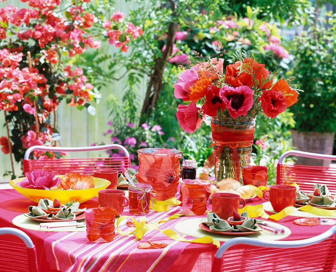 Summery table set with poppies in glass vases and a water bowl and hurricane candles with flower petals