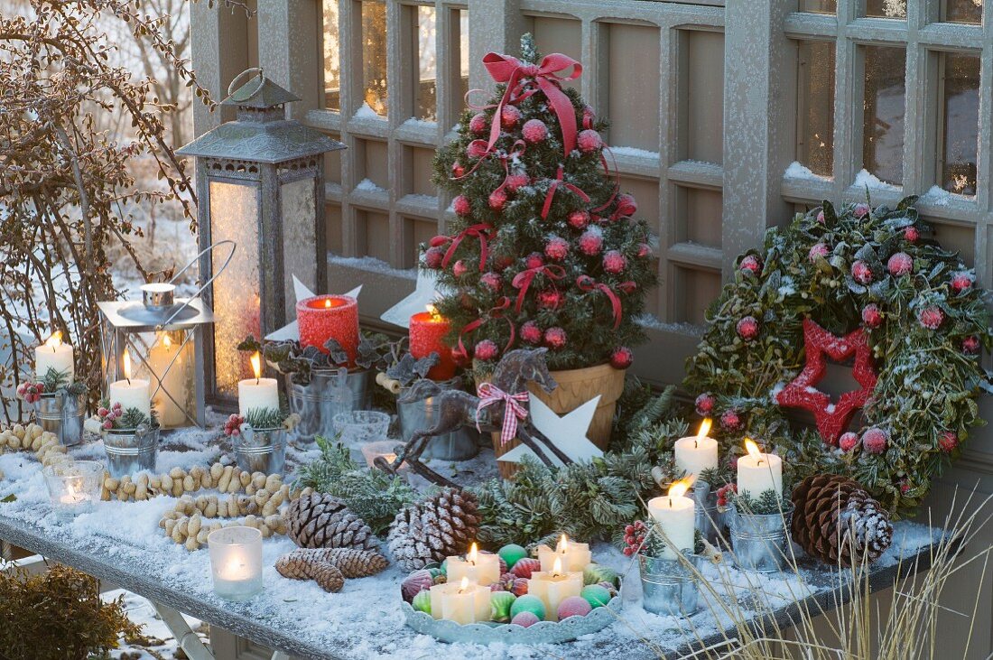 Weihnachtliches Tischarrangement mit geschmückter Zuckerhutfichte, Kranz, Laternen, Kerzen und Zapfen