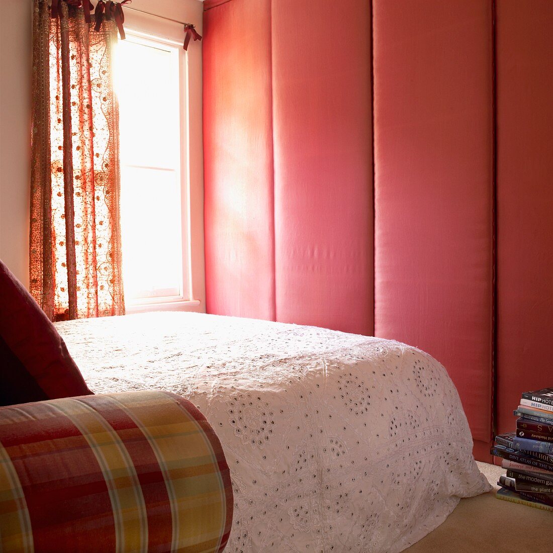 Schlafzimmer mit stoffbezogenem Schrank, Doppelbett mit Tagesdecke und Fenster mit gemusterten Vorhängen